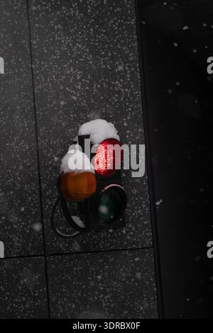 Nahaufnahme einer kleinen Ampelanlage an einem Ausgang der Tiefgarage bei Schneefall. Rote Leuchte leuchtet, Schnee bedeckt das Signalgehäuse Stockfoto