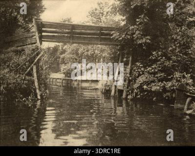 Dieses Foto von Adriaan Boer aus dem Jahr 1915 zeigt die alte Brücke in Giethoorn, Niederlande, die einen Kanal überspannt. Die Holzstruktur, typisch für die niederländische ländliche Architektur, befindet sich in einem Dorf mit Wasserstraßen und traditionellen Häusern. Das Bild dokumentiert das Dorfleben des frühen 20. Jahrhunderts, die ländliche Landschaft und das niederländische architektonische Erbe und spiegelt bildhafte Techniken und die visuelle Kultur der ländlichen Niederlande wider. Stockfoto