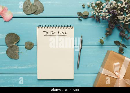 Sammlung von Gegenständen auf blauem Tisch mit Notizblock, Stift, Blumen und Geschenk Stockfoto