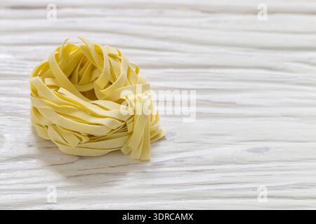 Agliatelle. Traditionelle italienische hausgemachte rohe Nudeln auf weißem Holzhintergrund aus nächster Nähe. Nester Stockfoto