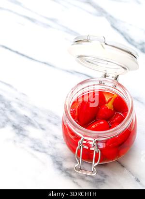Rote, heiße Chili-Paprika. Piri piri. Eingelegte Paprika in einem Glasgefäß auf einem Marmortisch. Ein Gourmet-Snack für Fleisch und Geflügel. (Kapsisch Stockfoto