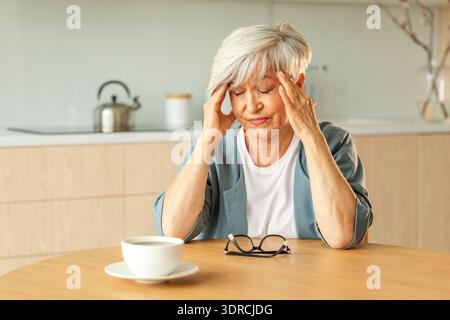 Kopfschmerzen, unglückliche Seniorin mittleren Alters, die an Kopfschmerzen leidet, krank, die Schläfen zu Hause reibt. Reifer alter Seniorengroßmot Stockfoto
