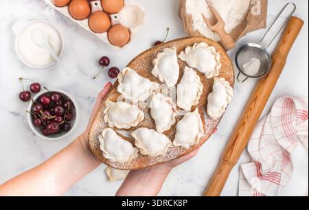 Bereiten Sie köstliche süße Teigtaschen mit Kirschen zu. Traditionelles russisches und ukrainisches Dessert. Vareniki und Zutaten auf dem Merb Stockfoto
