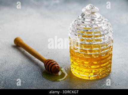 Flüssiger Blütenhonig in einem Glas mit Holzhonigtaube auf Beton- oder Steingrund. Selektiver Fokus, Kopierbereich Stockfoto