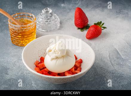 Gourmet-Burrata-Käse mit Erdbeertartar und Honig in einer Leuchtplatte auf grauem Beton- oder Steinhintergrund. Frühstück. De Stockfoto