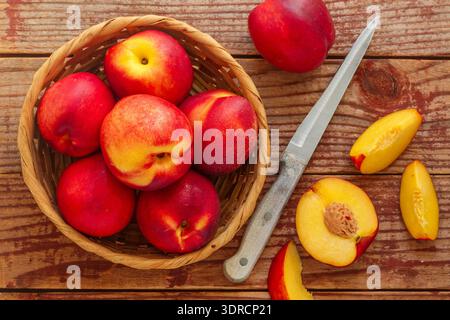 Nektarine. Reife saftige Bio-Nektarinen (Pfirsiche) in einem Korb. Ganze und geschnittene Früchte auf einem Holztisch. Selektiver Fokus Stockfoto
