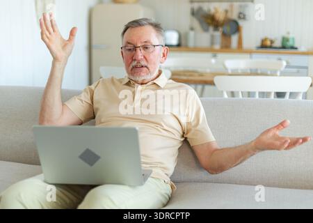 Ein glücklicher älterer Mann mittleren Alters mit Laptop spricht mit Freunden und Familie über Videogespräche. Reifer alter Großvater, der Spaß hat, zu reden Stockfoto