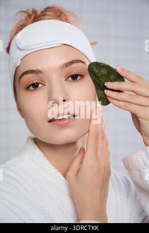 In einem sanft beleuchteten Raum trägt eine junge Frau einen grünen Stein auf ihre leuchtende Haut. Stockfoto