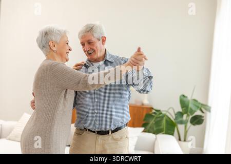 Bleiben Sie in Bewegung. Ein romantisches älteres Ehepaar, das zu Hause zu Musik tanzt. Glücklich lächelnde Familie Rentner Frau Ehemann Ehefrau Stockfoto