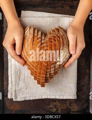 Geschnittener runder Roggenbrot in Herzform auf einer grauen Leinenserviette in Kinderhänden. T Stockfoto