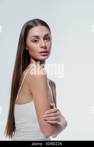 Die schöne junge Frau steht elegant und zeigt ihr langes Haar vor einem ruhigen Hintergrund. Stockfoto