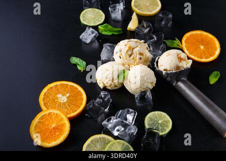 Verschiedene Früchte und Eiskugeln auf einem schwarzen Tisch Stockfoto