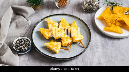 Gefälschte Weihnachtsbäume aus Dreieckskäse in Nacho zerbröckeln auf einem Teller-Webbanner Stockfoto