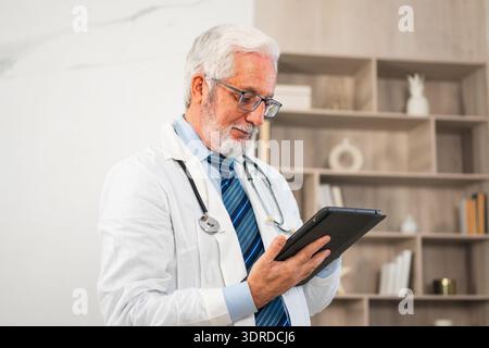 Reifer Senior männlicher Arzt in medizinischer Uniform mit digitaler Tablette in der Klinik, Therapeut professionelle Gesundheitsexperte suchen Stockfoto