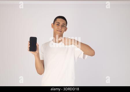 Junger Mann in weißem T-Shirt, der auf sein Smartphone zeigt Stockfoto