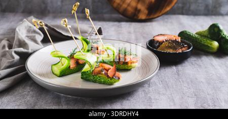 Herzhafte Vorspeise mit frischen Gurken, geräuchertem rotem Fisch auf einem Teller auf dem Tischbanner Stockfoto