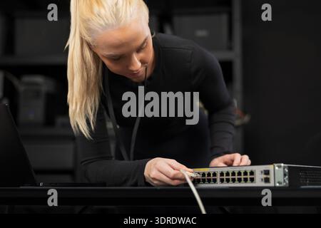 Professionelle IT-Technikerin, die einen Netzwerk-Switch in einer modernen Büroumgebung konfiguriert Stockfoto
