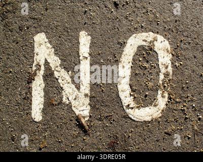 Nahaufnahme des Wortes NO in weißer Farbe auf dunkler, grauer Asphaltoberfläche, die eine klare Botschaft des Verbots oder der Ablehnung vermittelt, Best.-Nr. Stockfoto