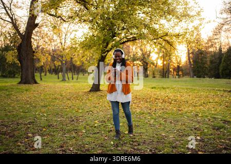 Junge Frau, die Musik über Kopfhörer im Herbstpark genießt Stockfoto