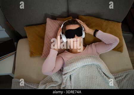Frau, die sich im Bett entspannt und Musik mit Schlafmaske hört Stockfoto