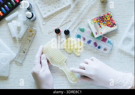 Weibliche Hände in Handschuhen halten eine Form für die Herstellung eines Kamms aus Epoxidharz Stockfoto