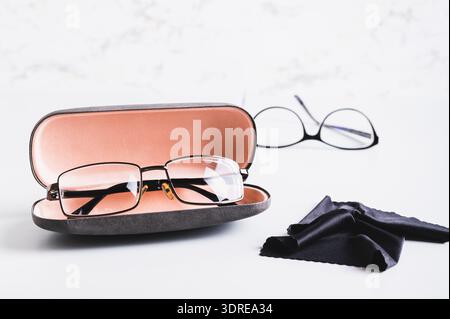 Brille in einem offenen Hartschalenkoffer und ein Reinigungstuch vor anderen Gläsern auf einem Tisch Stockfoto