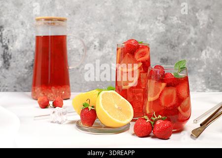 Erdbeere Iced Tea oder Minze Lemon Cocktail ist ein erfrischendes Sommergetränk. Gläser mit Beeren-Frucht-Limonade auf einem Lichtkrug Stockfoto