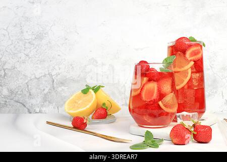Der Smoothie mit Eiserdbeeren oder Minze-Zitronen ist ein erfrischendes Sommergetränk. Glas mit Beerenfrucht-Limonade auf einem hellen Konkr Stockfoto