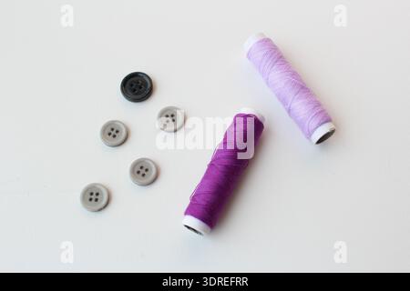 Nähset mit bunten Fadenspulen und Kunststoffknöpfen auf weißem Hintergrund. Perfekt für Handwerk, Schneiderei, heimwerkermode und Schneiderwerkzeuge. Stockfoto