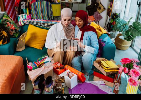 Zwei muslimische Unternehmerinnen sitzen zusammen, schauen sich eine stilvolle orange Handtasche an und diskutieren über neue Modeprodukte für ihre kleine Online-E-Kommunikation Stockfoto