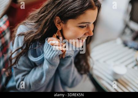 Teenager lächelt in einem gemütlichen blauen Strickpullover in einem Café im Freien Stockfoto