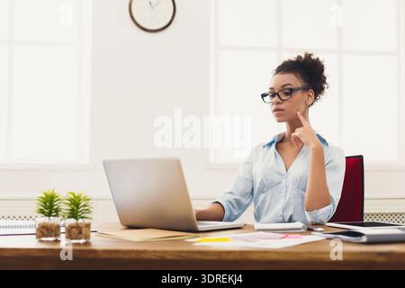 Frau, die tagsüber am Schreibtisch im hellen Büro arbeitet und über Projektdetails nachdenkt Stockfoto