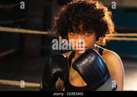 Aufschrei unabhängiger Mädels Macht. Wütende afroamerikanische Kämpferin mit Boxhandschuhen, die ziemlich aggressiv aussehen, auf bo zu stehen Stockfoto