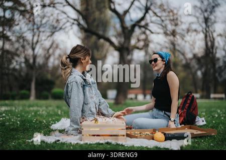 Zwei Frauen genießen ein entspanntes Picknick im Park, teilen sich Pizza und lachen zusammen Stockfoto