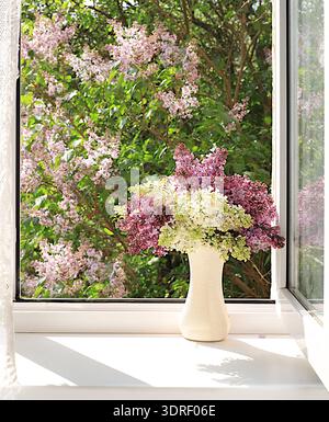 Blumenstrauß mit Frühlingslila-Blüten in einer Vase auf einem sonnigen Fenster, abstraktes Blumenarrangement, Stillleben mit blühendem Baumzweig Stockfoto