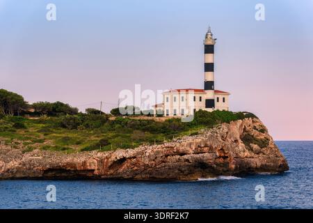 Ein schwarz-weiß gestreifter Leuchtturm steht an einer felsigen Küste über dem Mittelmeer in Portocolom, Mallorca, Spanien Stockfoto