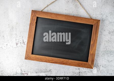 Leere schwarze Tafel oder Schultafel, die an einer Steinwand hängt. Leere dunkelbraune Motivationsbotschaft aus Holz. Stockfoto