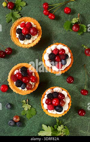 Leckere Tartlets mit frischen Beeren Himbeeren, Kirschen, Stachelbeeren und Heidelbeeren. Cupcakes mit weicher Quark Creme, Sommer Stockfoto
