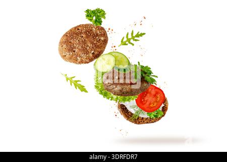 Sandwich Toast mit gegrilltem Rindfleischkotelett und frischen Kräutern und Gemüse, die isoliert auf weißem Hintergrund fliegen. Rindfleisch Patty Burger Zutaten fallen Stockfoto