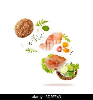 Offenes Sandwich Toast mit traditionellen spanischen Jamonschinkenscheiben (getrocknetes Schweinefleisch) und frischen Kräutern und Gemüse, die isoliert auf weißem Hintergrund fliegen. Stockfoto