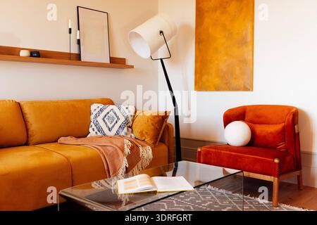 Stilvolle, moderne Wohnzimmereinrichtung. Elegante Stehlampe und weiches helles Sofa mit Sessel. Öffnen Sie das Buch auf dem Glastisch. Nat Stockfoto