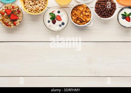 Frühstückskollektion in Schüsseln mit verschiedenen Müsli- und Cornflakes, Obst und Joghurt auf einem Holztisch Stockfoto