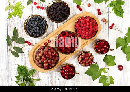 Sommer frische Beeren, Kirschen, Brombeeren, Stachelbeeren, Heidelbeeren und Himbeeren auf einem hölzernen Hintergrund mit Blättern, bann Stockfoto