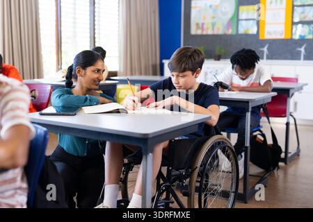 In der Schule half eine indische Lehrerin dem Jungen im Rollstuhl beim Schreiben im Klassenzimmer Stockfoto