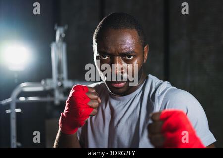 Boxer im Fitnessstudio. Aggressiver Afrikanerkämpfer, der sich nach dem Training im Boxen ausruht, bereit für den Kampf, mit Blick auf die Kamera. Stark geschwitzter Mann Stockfoto