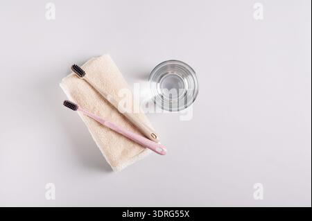 Zwei Zahnbürsten auf einem Handtuch und ein Glas Wasser auf grauem Hintergrund, Draufsicht Stockfoto