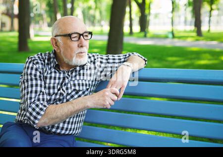 Ein älterer Mann sitzt nachmittags auf der Blue Bench in Park, verloren in Gedanken und Nachdenken Stockfoto