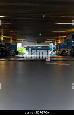 Tiefgarage mit geparkten Autos, Betonboden, Deckenbeleuchtung, blauer Beschilderung und Richtungspfeilen Stockfoto