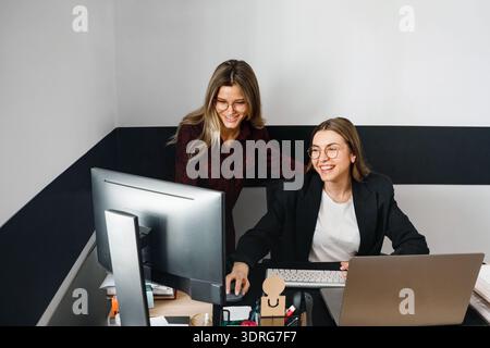 Zwei Frauen beschäftigen sich am Schreibtisch mit Computern, diskutieren tagsüber Arbeitsaufgaben und tauschen Ideen im Büro aus. Stockfoto