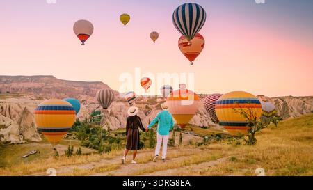 Ein Paar erlebt einen magischen Sonnenaufgang in Kappadokien mit Heißluftballons, die über ihnen schweben Stockfoto